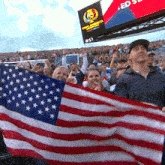 a group of people holding an american flag in front of a scoreboard that says ' ed ' on it