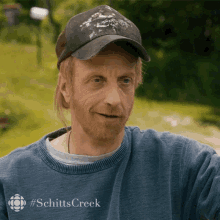 a man wearing a hat and a blue sweater with #schitts creek written on it