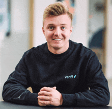 a man wearing a veriff sweatshirt sits at a table with his hands folded