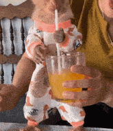 a baby wearing a chanel outfit drinks from a glass