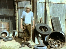 a man with white hair is standing in front of a building surrounded by tires and barrels .