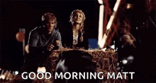 a man and a woman are sitting on a bale of hay and the man is saying `` good morning matt '' .