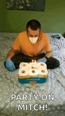 a man wearing a mask and gloves is sitting on a bed with a birthday cake made out of toilet paper rolls