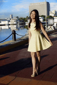 a woman in a yellow dress is standing on a sidewalk near a body of water