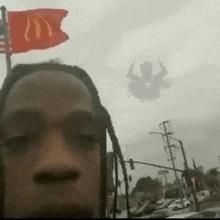 a man with dreadlocks is taking a selfie with a mcdonald 's flag flying in the background .