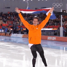 a man in an orange jacket holds a flag over his head in front of a sign that says sochi 2014