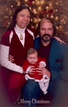 a man and woman are holding a baby in front of a christmas tree in a christmas card .