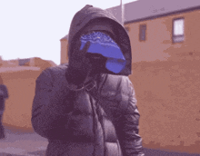 a man wearing a bandana and a hooded jacket is standing in front of a building .