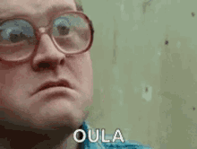 a man wearing glasses and a blue shirt is making a funny face and saying oula .