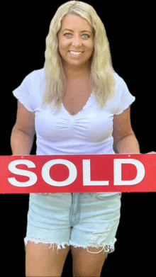 a woman is holding a sold sign in her hands