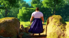 a woman in a blue skirt is walking between two large rocks in a forest .