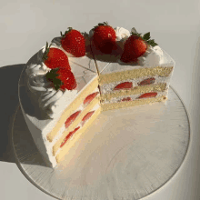 a strawberry cake with whipped cream and strawberries on top is cut in half on a glass plate .