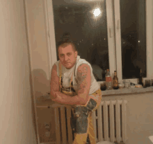 a man with a tattoo on his arm is leaning on a radiator next to a window