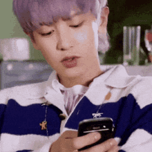 a man with purple hair is holding a cell phone in his hand .