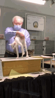 a man in a blue shirt holds a white cat in front of a sign that says the cat fanciers association