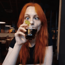 a woman with red hair is drinking from a glass