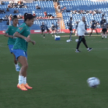 a woman kicking a soccer ball on a field with a stadium in the background that says ' nissan '