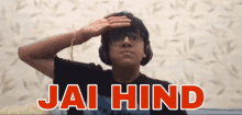 a man wearing headphones salutes in front of a wall that says " jai hind "