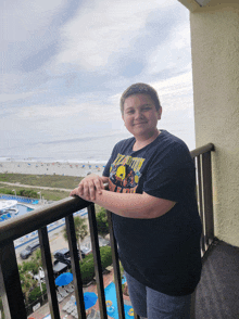 a boy standing on a balcony wearing a shirt that says ' simpson ' on it