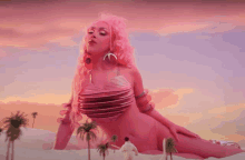 a woman with pink hair is laying on her stomach with palm trees in the background