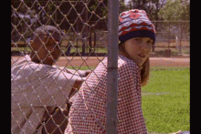 a boy and a girl are behind a chain link fence and the girl is wearing a hat with the number 8 on it