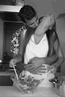 a man is kissing a woman on the neck while she prepares a salad .