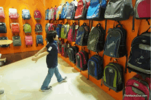 a boy stands in front of a wall full of backpacks including one that says ' explorer ' on it