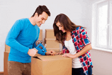 a man in a blue shirt tapes a box while a woman in a plaid shirt looks on