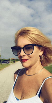 a woman wearing sunglasses and a white tank top is standing on a road