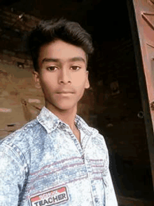 a young man in a denim shirt is standing in front of a door and taking a selfie .