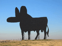 a large silhouette of a cow in a field with a blue sky behind it