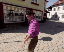 a man in a pink plaid shirt walks down a cobblestone street in front of a store that says rollladen