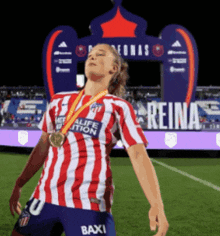 a woman wearing a red and white striped shirt with a medal around her neck stands on a soccer field