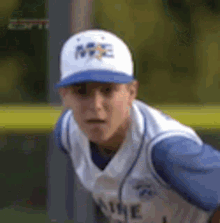 a young man wearing a baseball cap and a blue and white jersey is standing on a baseball field .