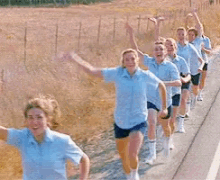 a group of women in blue shirts and shorts are running down a road with their arms in the air