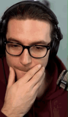 a man wearing glasses and headphones is covering his mouth with his hand