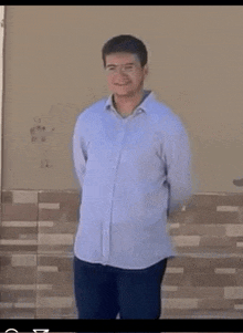 a man wearing a blue shirt and black pants is standing in front of a wall .