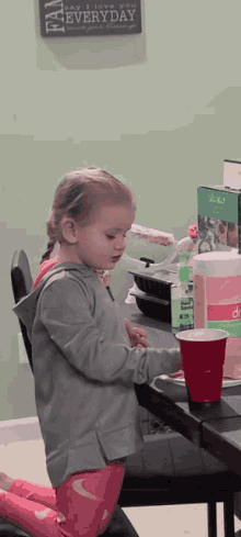 a little girl sits at a table in front of a sign that says " say i love you every day "