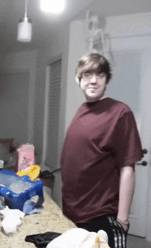 a man in a maroon shirt stands in front of a kitchen counter