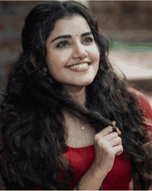 a woman with long curly hair wearing a red top smiles