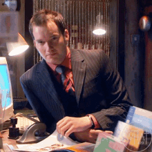 a man in a suit sits at a desk in front of a computer and a sign that says what 2020