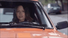 a woman is driving a red car down a street .