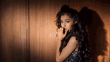 a woman with curly hair is standing in front of a wooden wall and covering her mouth with her hand .