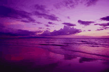 a purple sunset over a beach with waves crashing on the shore