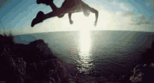 a man is jumping over a cliff into the ocean .