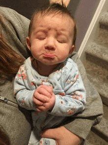 a woman is holding a baby in her arms and the baby is making a funny face .