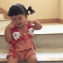 a little girl wearing a mickey mouse glove is sitting on a set of stairs with her eyes closed