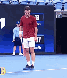 a man in a red shirt is holding a tennis racquet on a tennis court in front of a sign that says 13