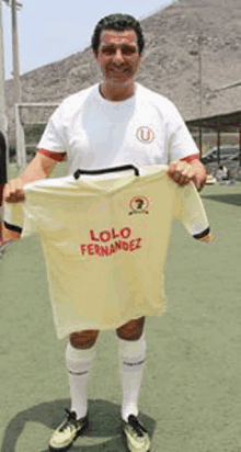 a man in a white shirt is holding a yellow shirt with the name lolo fernandez on it