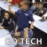 a young boy is standing on a chair in a classroom while a group of children sit at tables .